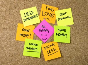Group of New year Resolutions Post it Notes on pink, yellow, orange and green on cork board written with message of diet, join gym, find love, quit smoking and be happy