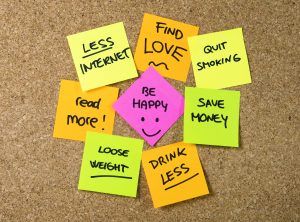 Group of New year Resolutions Post it Notes on pink, yellow, orange and green on cork board written with message of diet, join gym, find love, quit smoking and be happy